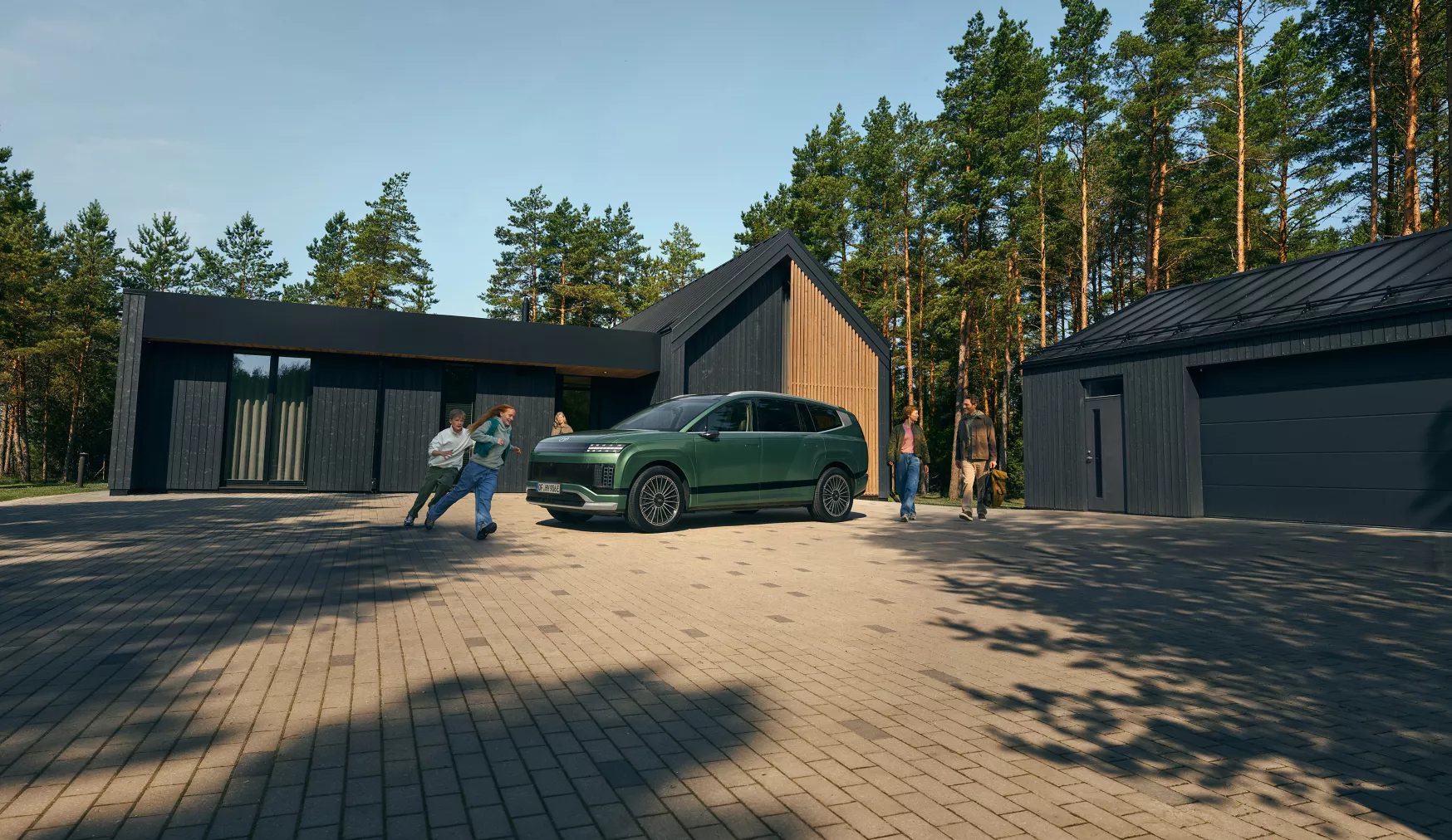 Grön Hyundai IONIQ 9 framför ett modernt hus med familj runt bilen