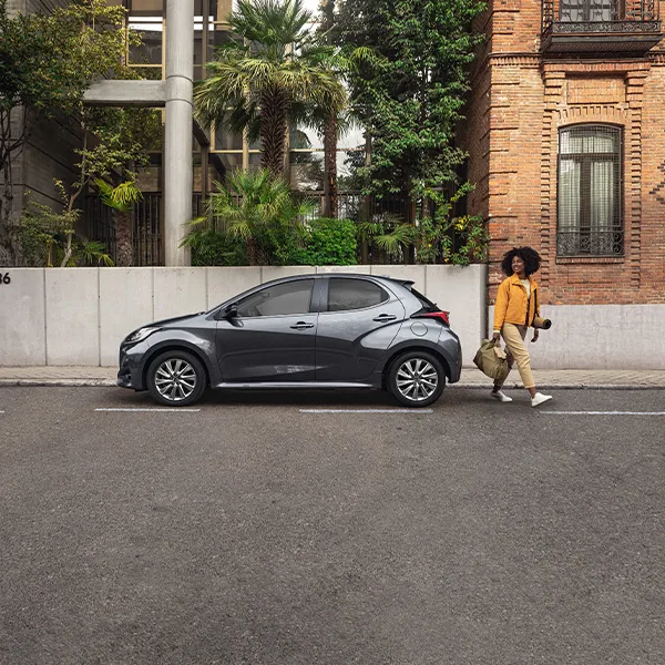 Kvinna går från sin gråa Mazda2 Hybrid