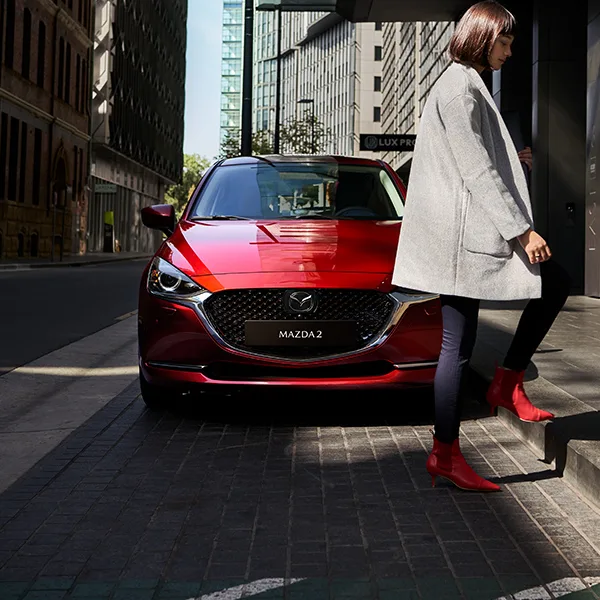 Kvinna med röda skor går framför en röd Mazda2