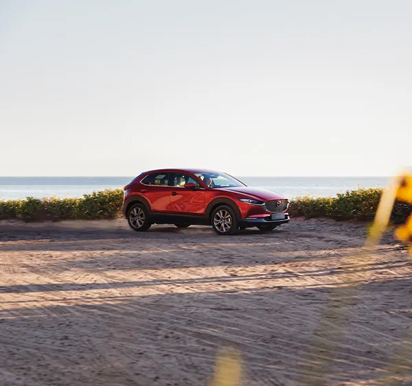 Röd Mazda CX-30 parkerad vid stranden och havet som bakgrund