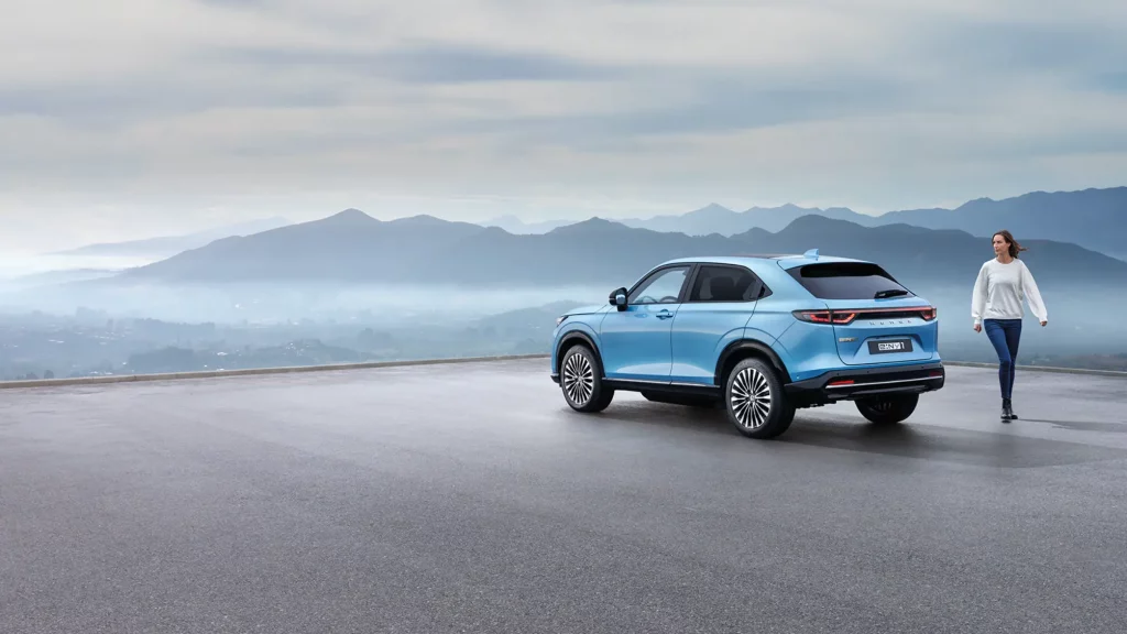 Blå Honda e:Ny1 parkerad vid plattform med utsikt över bergen och en tjej går brevid