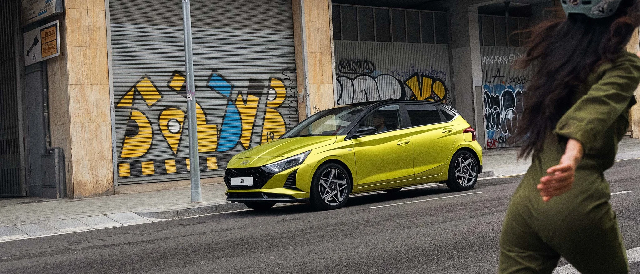 Hyundai i20 i färgen Lucid Lime parkerad längs gat i city med grafitti i bakgrunden