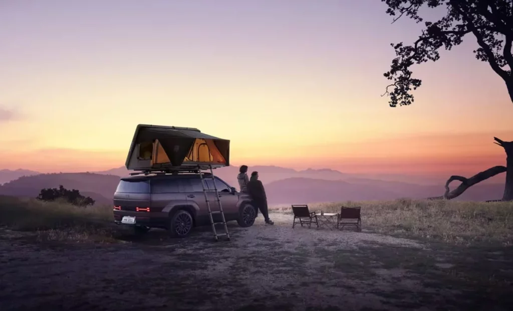 Helt nya SANTA FE Plug-in Hybrid i kopparfärg med taktält och par som lutar mot bilen och kollar på solnedgången över ett bergsparti