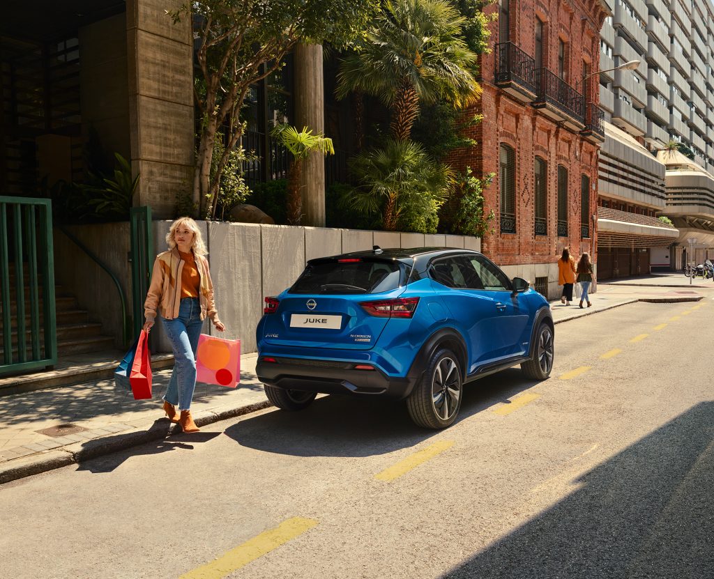 Kvinna går med shoppingkassar bakom en blå Nissan Juke