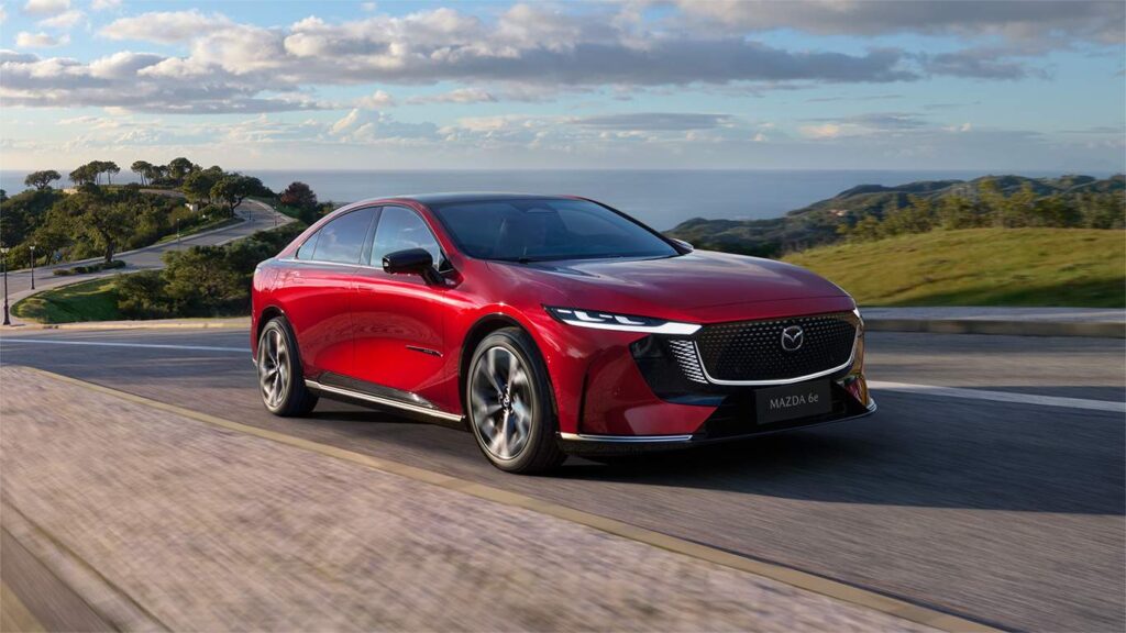 Nya MAZDA 6e elbil i röd färg åker på en landsväg längs med vattnet